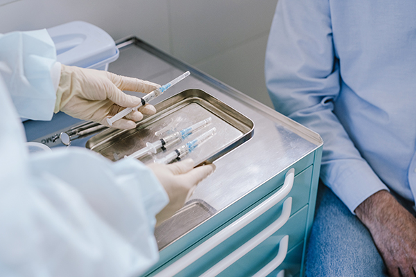 Pre-filled Syringes on tray counter in medical office. Medical professionals in scrubs are handling the syringes in front of a patient.